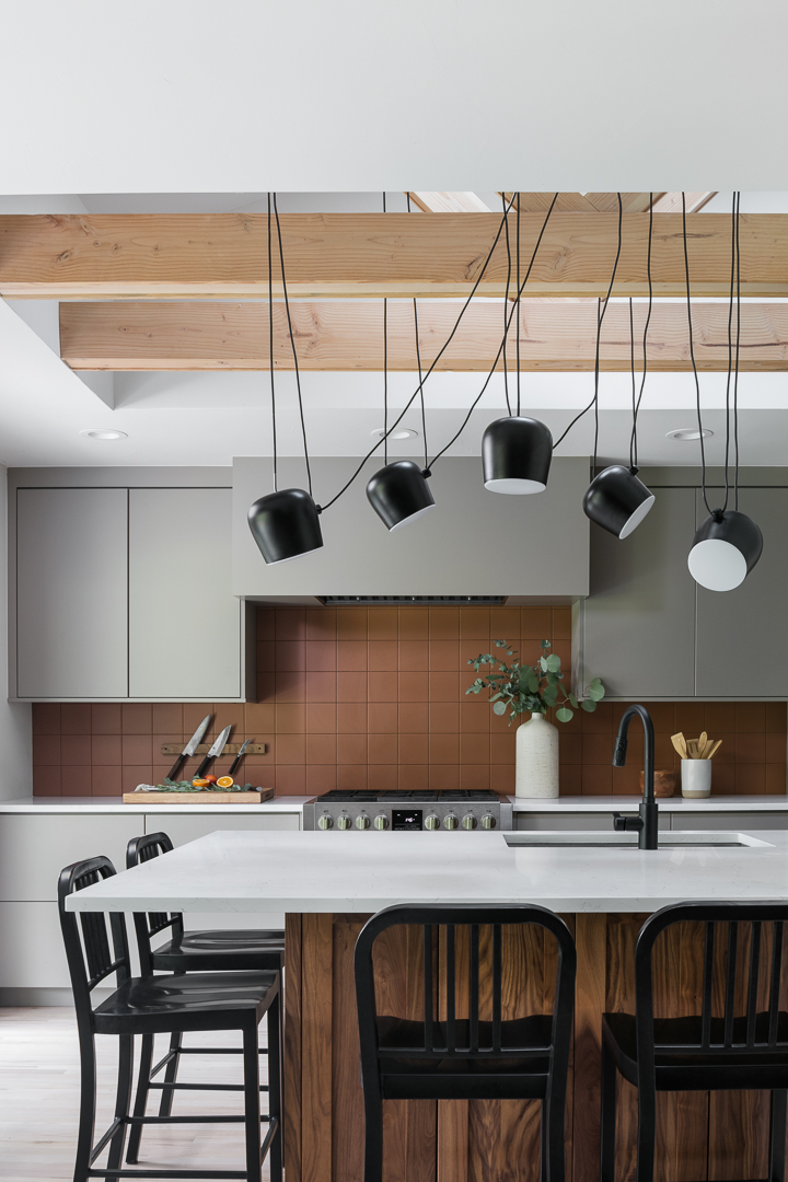 Kitchen with gray cabinetry, a copper tile backsplash, and black pendant lights in The Alford Dwelling renovation by Forge & Bow