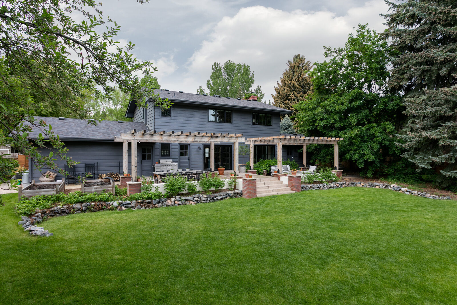 Backyard patio with a wood pergola and stone paving in The Dartmouth House renovation by Forge & Bow