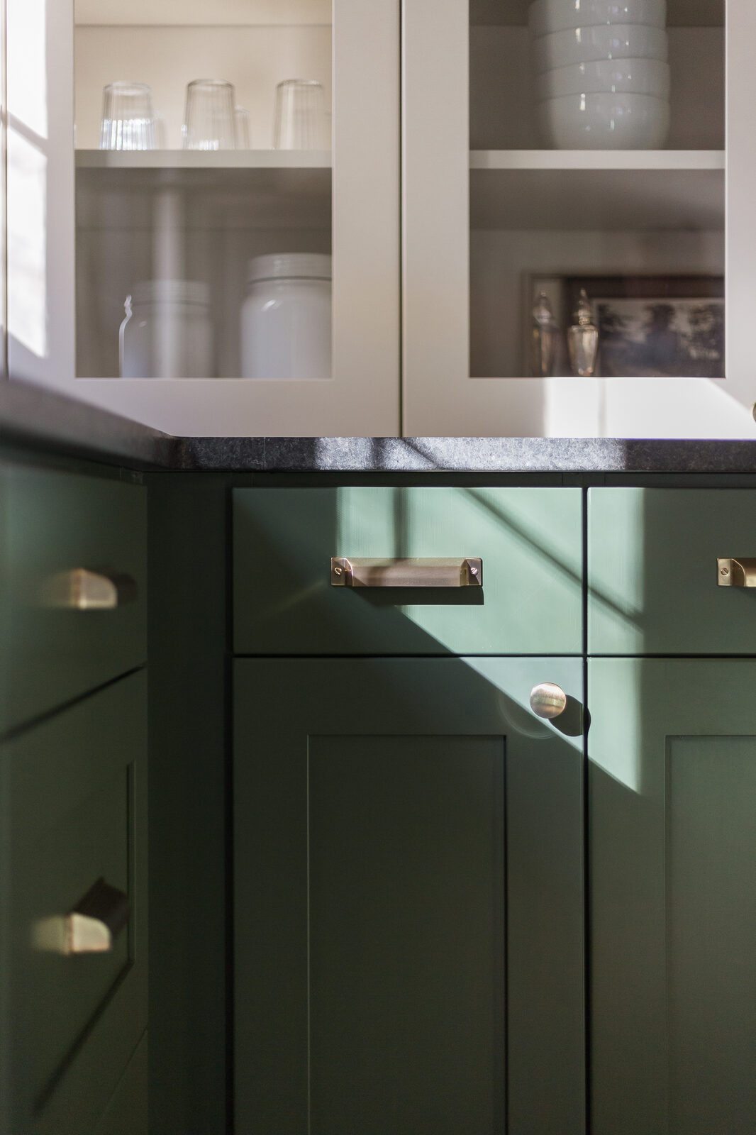 Detail of dark green cabinetry with brass hardware and a black soapstone counter in The Mulberry House renovation by Forge & Bow