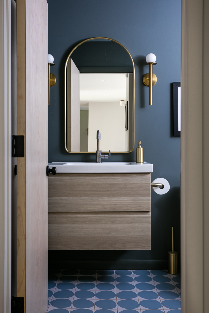 Powder bathroom with a floating wood vanity and brass arched mirror in The Alford Dwelling renovation by Forge & Bow