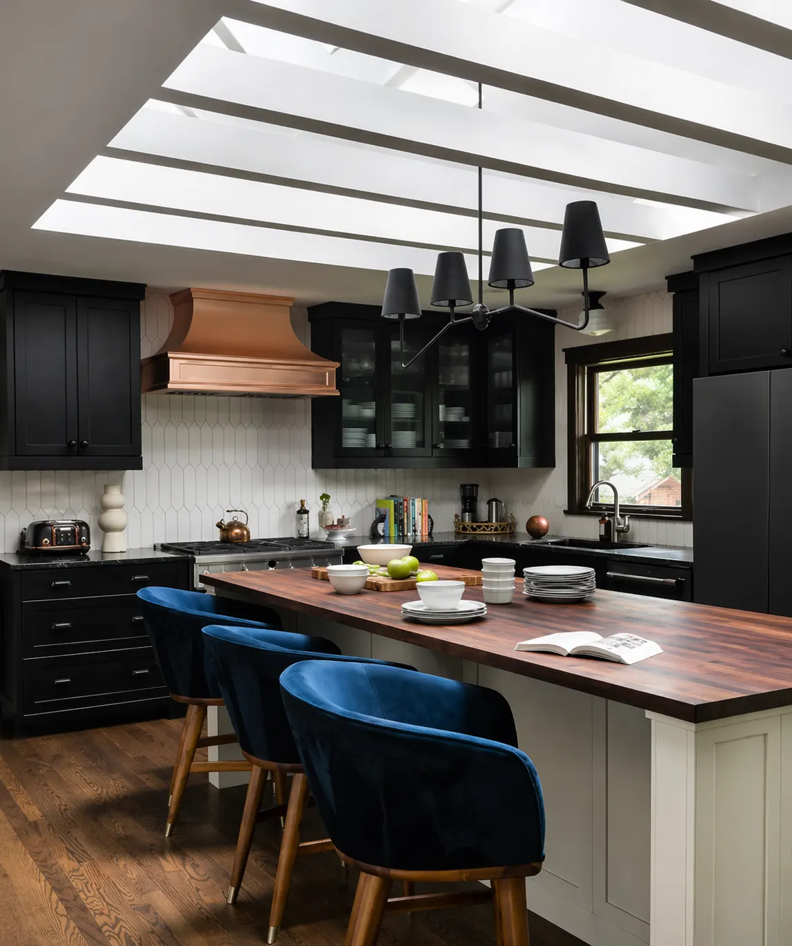 Kitchen with a skylight, black cabinetry, a copper range hood, and navy velvet counter stools in the Seminole renovation by Forge & Bow