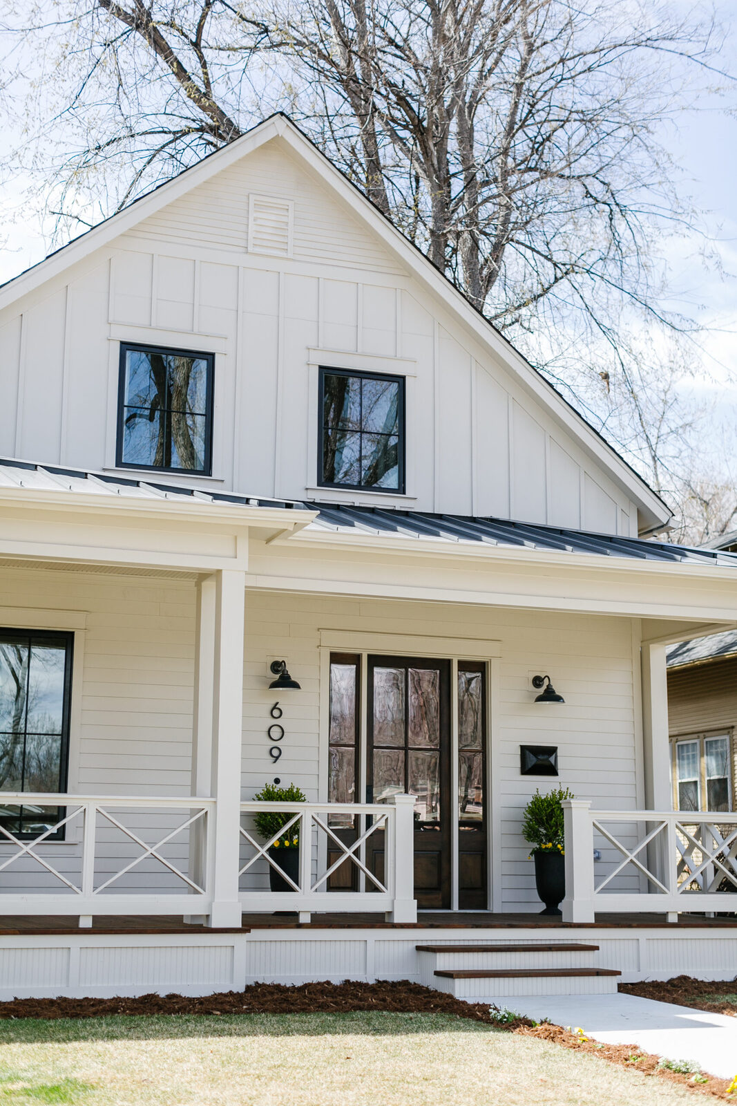 Exterior of the white farmhouse with a black metal roof and wraparound porch, a Forge & Bow new build
