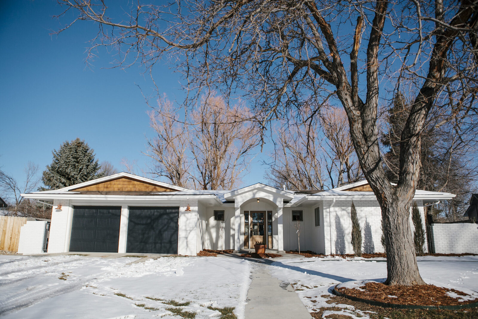 Snowy exterior of a stucco ranch home with black garage doors, a Forge & Bow project
