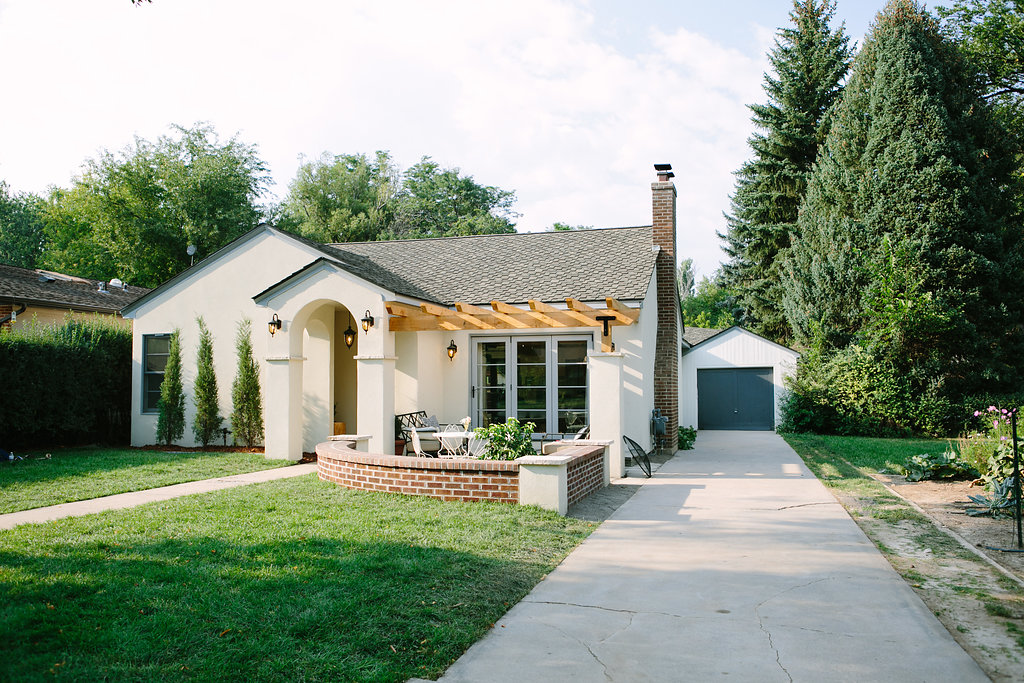Exterior of the white stucco bungalow with an arched entry and brick planter in The Buckeye Dwelling renovation by Forge & Bow