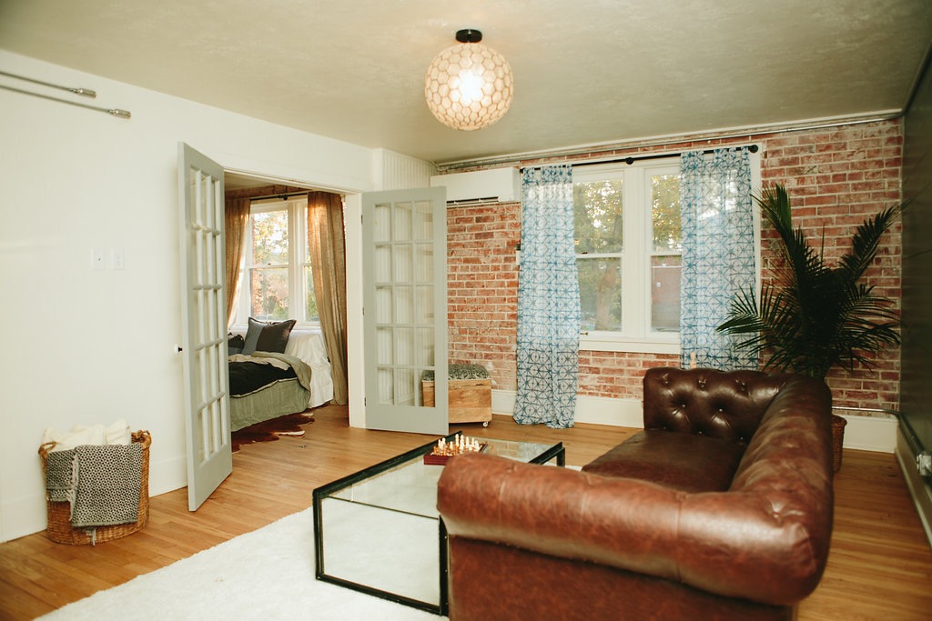 Living area with exposed brick walls and a leather chesterfield chair in The Laurel Apartments renovation by Forge & Bow