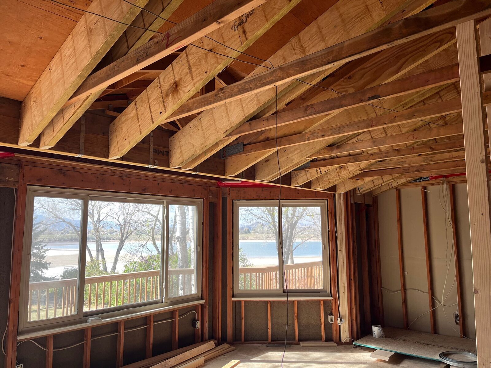 Exposed roof trusses during framing with a water view through the window, a Forge & Bow new build in progress