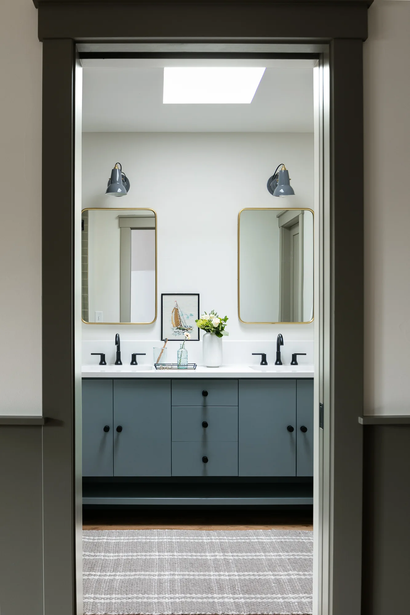 Primary bathroom with a slate blue double vanity and brass arched mirrors in The Mulberry House renovation by Forge & Bow