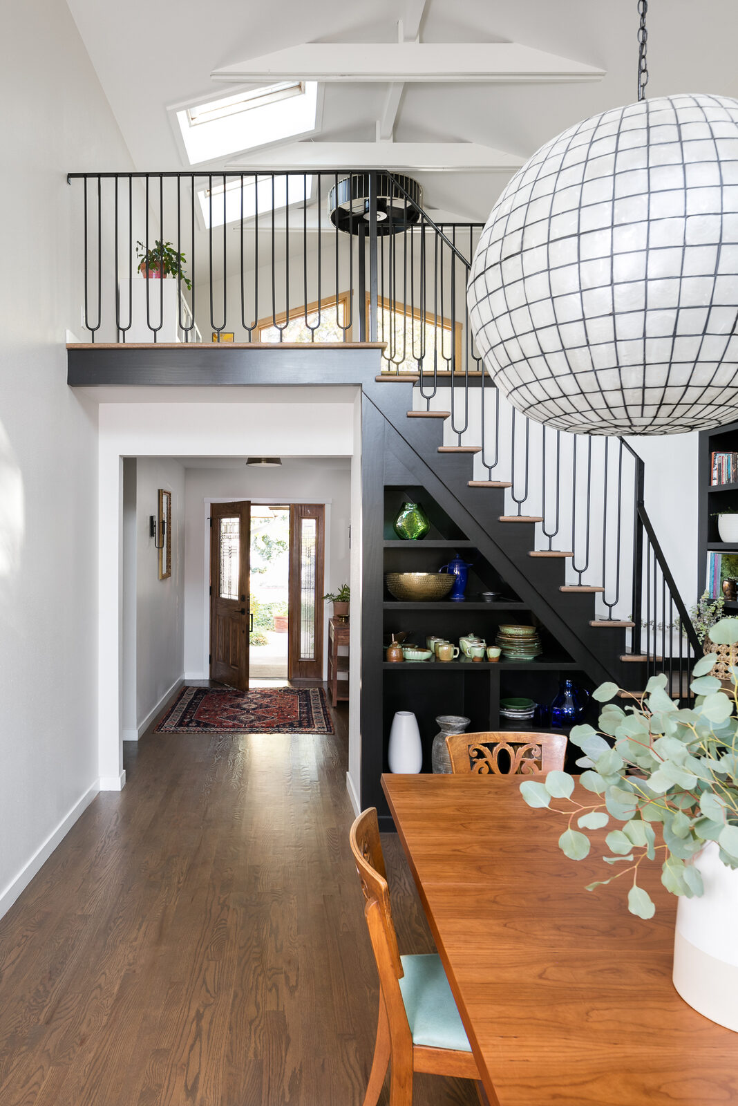 Dining nook with a loft railing and spherical paper pendant light in the Osage renovation by Forge & Bow