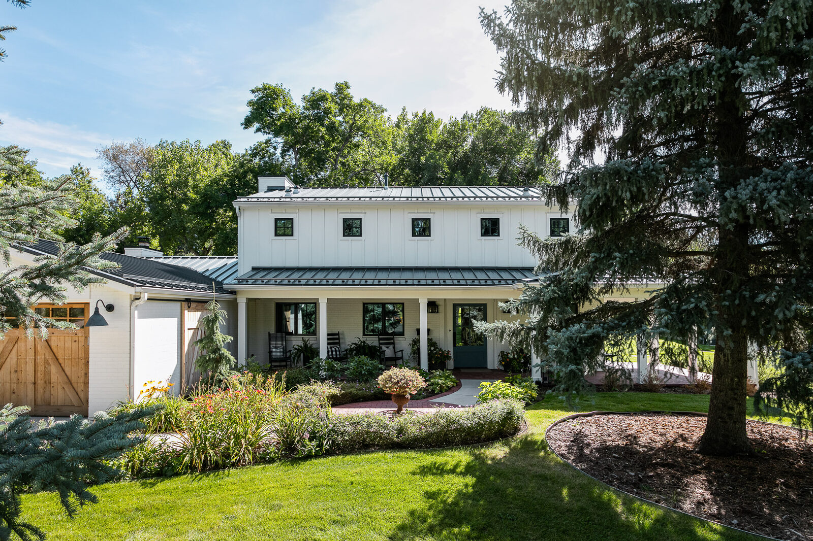 Exterior of the white farmhouse with a black standing-seam roof and wraparound porch in the Paradise Lane new build by Forge & Bow