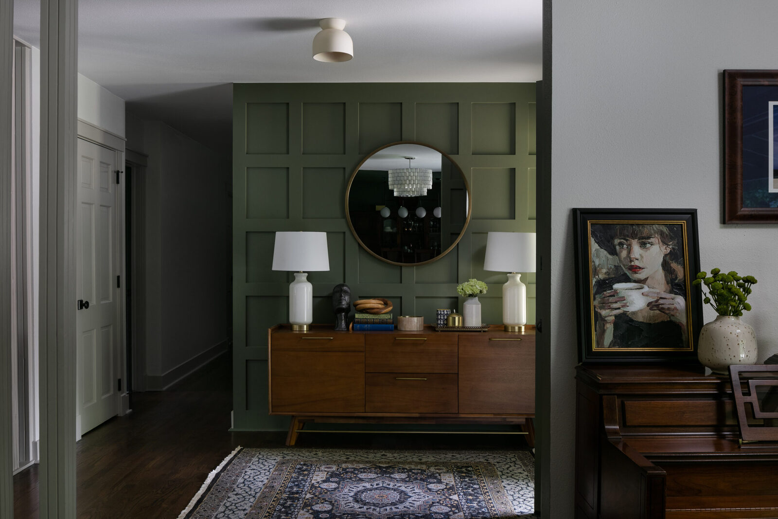 Entry with a dark green paneled wall, round mirror, and walnut console table in the Seminole renovation by Forge & Bow