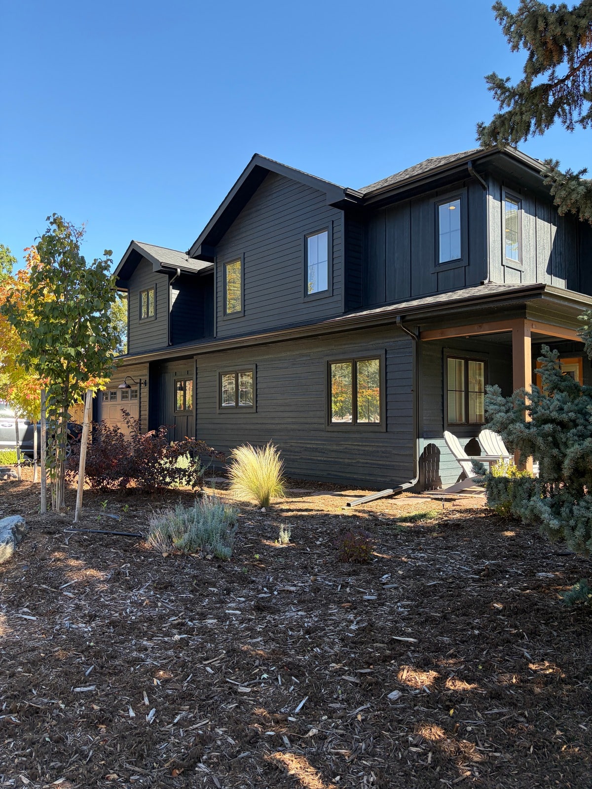 Exterior of the dark charcoal modern new build with wood porch posts and fall landscaping by Forge & Bow