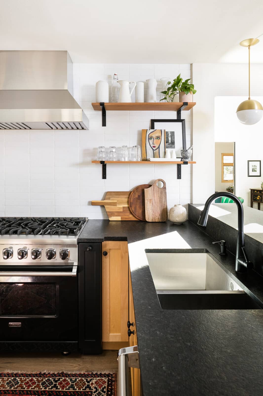 Kitchen counter and sink with black countertops, open shelving, and a brass pendant light in the Osage renovation by Forge & Bow