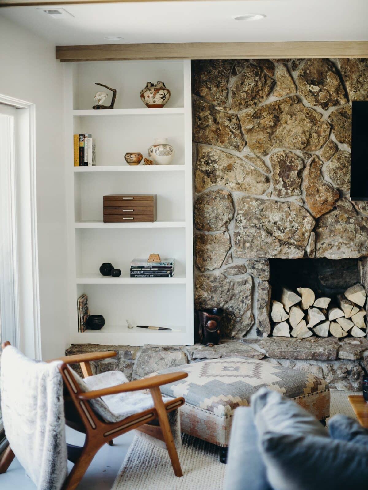 Living room with a natural stone fireplace wall and built-in white shelving in The Teakwood Dwelling renovation by Forge & Bow